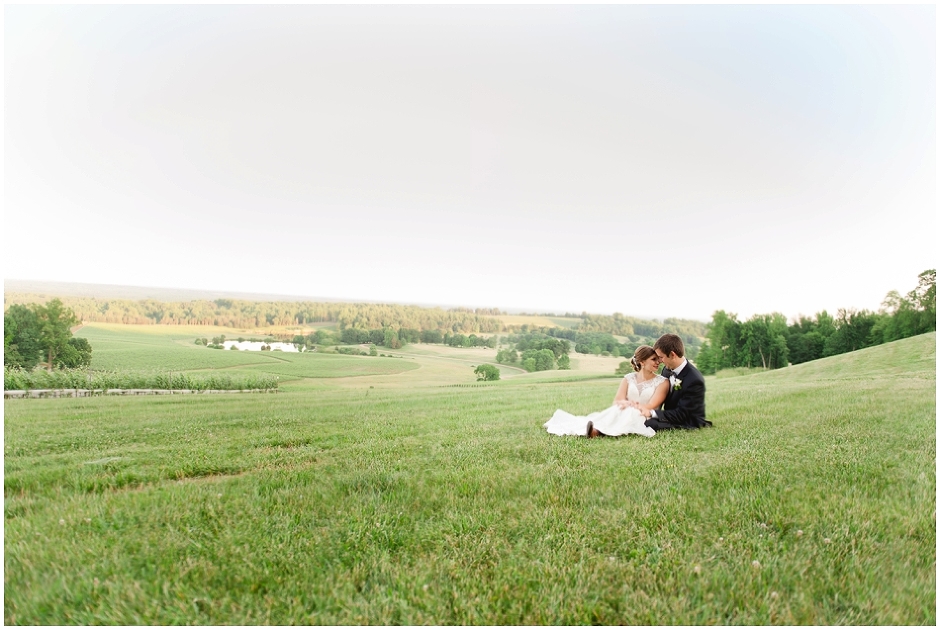 wedding couple sitting together on the grass with Albemarle mountains behind them by charlottesville winery wedding photographer